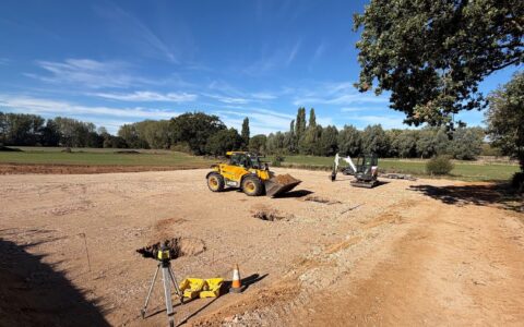 Foundation pads being dug for a new farm building on a hardcore base, with a telehandler, mini digger and laser level on site