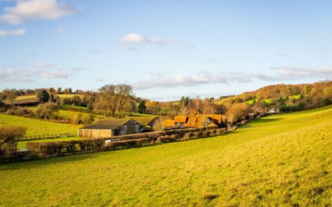 Farm buildings and a barn set among green grazing fields and rolling hills in the English countryside