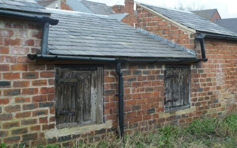 Disused brick agricultural building with boarded up windows and a slate roof on a UK farm, awaiting conversion
